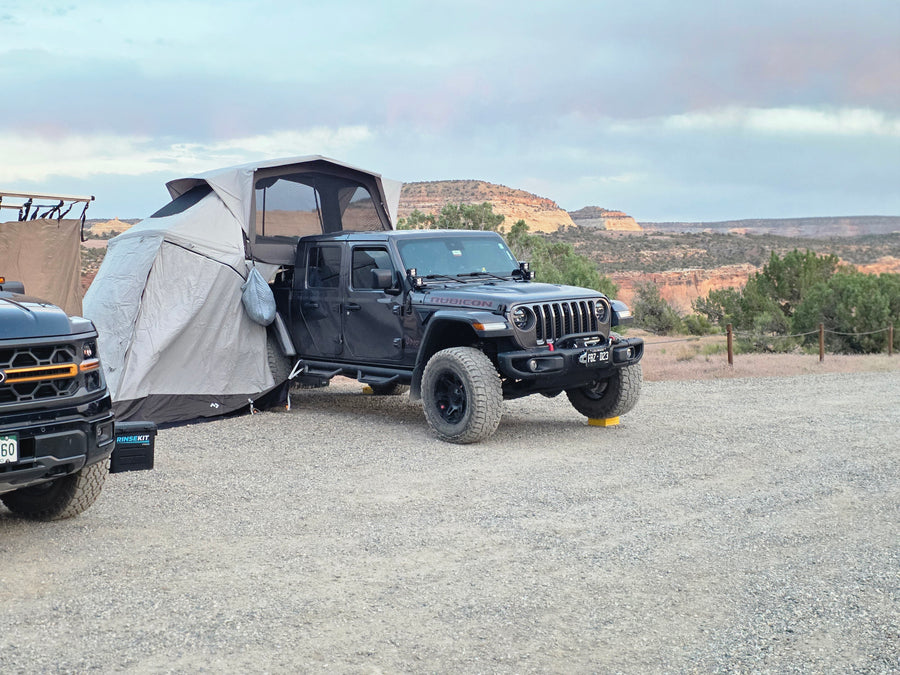An RV rental overlanding setup: a black Jeep Gladiator with a rooftop tent and annex, parked in a desert landscape.
