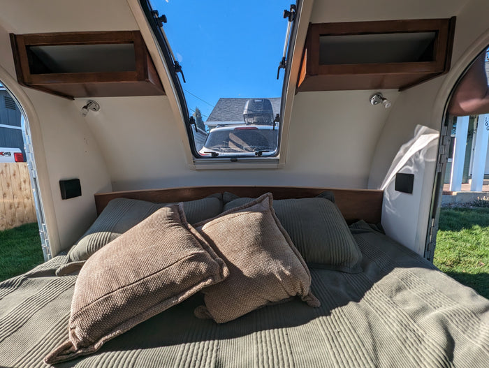 it awaits outdoor travel.|Inside a cozy RV rental: bed with blanket & pillows