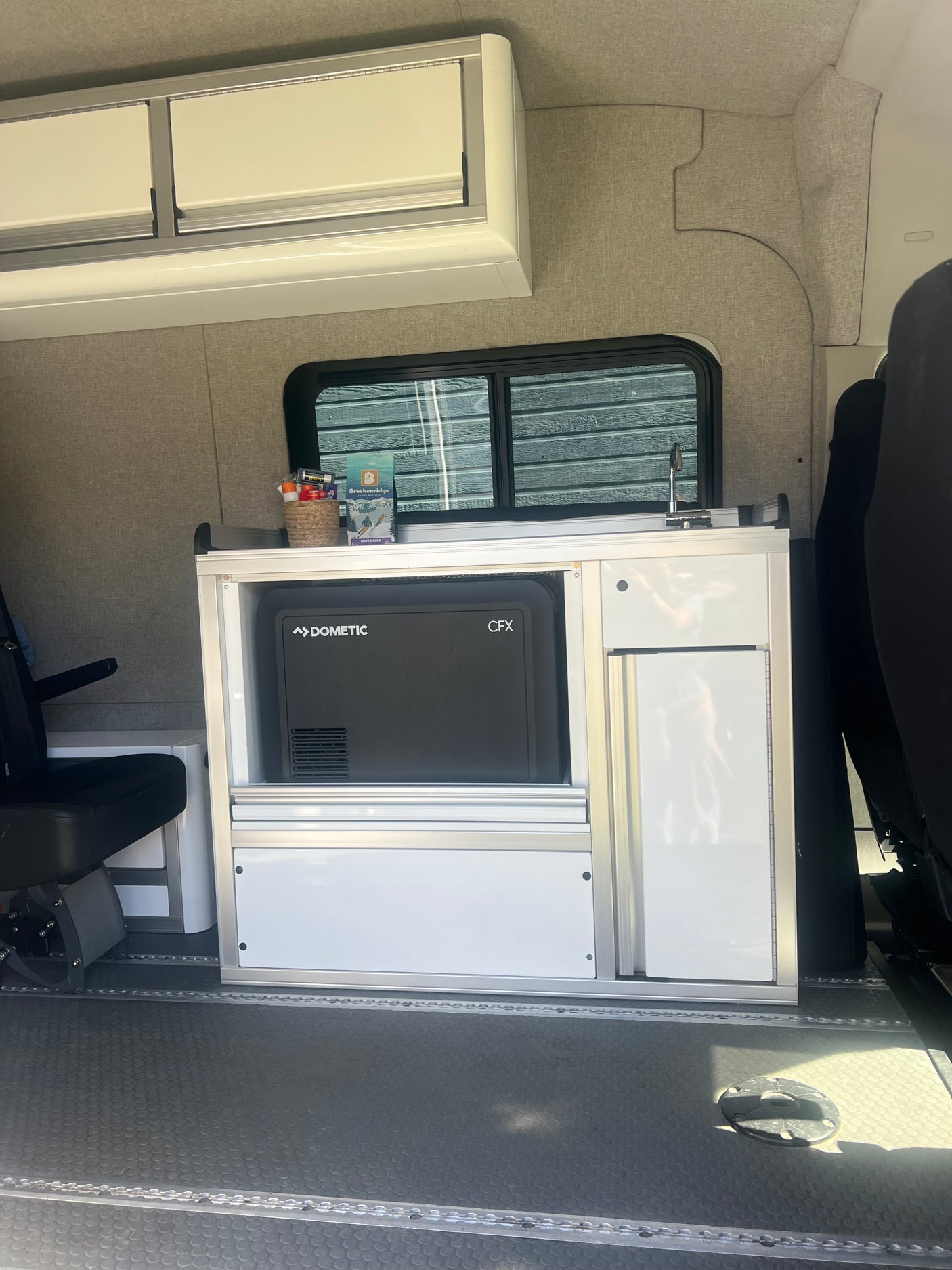 RV rental interior featuring a modular kitchen unit with a Dometic fridge, sink, and overhead storage cabinets.