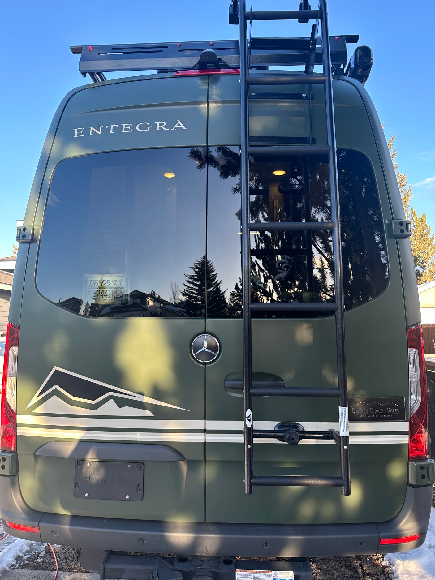 Rear of an olive green Mercedes-Benz Sprinter camper van, equipped with a roof rack and ladder, perfect for RV rental exploration.