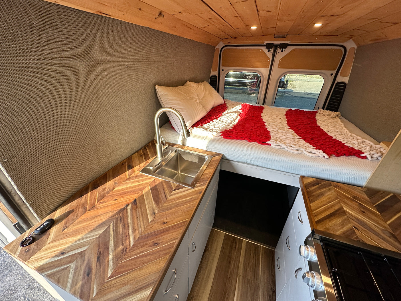 Cozy camper van interior for your next RV rental adventure, featuring a bed, kitchen, and wood finishes.
