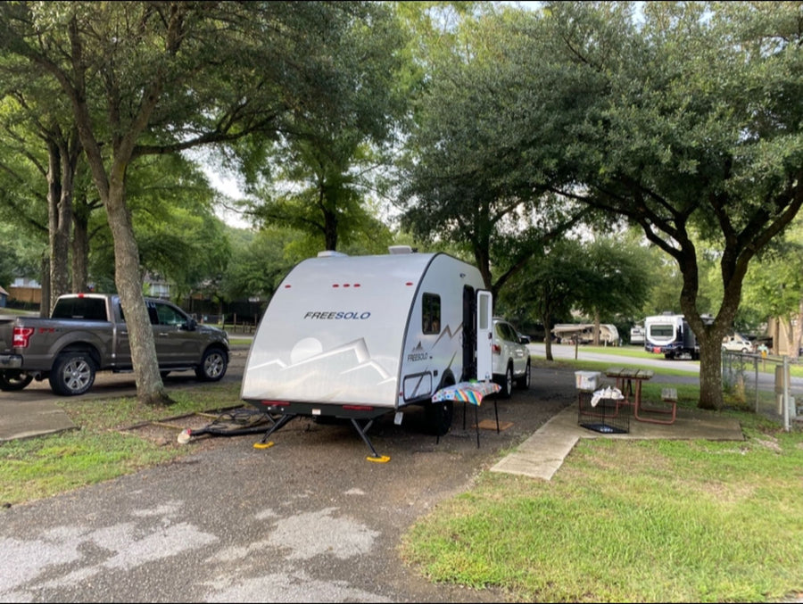 and gray pickup parked on red gravel with trees.|Grey Freesolo RV rental parked at a sunny campsite with outdoor amenities