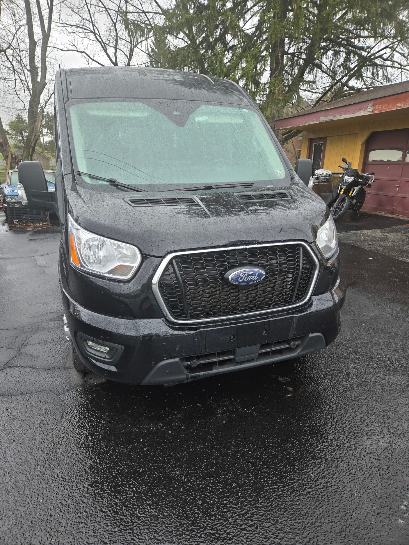 Black Ford Transit van, ideal for RV rental, wet from rain. Parked on a driveway, ready for your next trip.