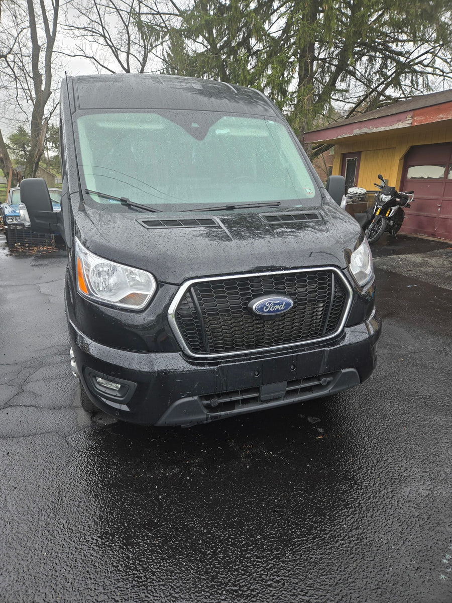 Black Ford Transit van, ideal for RV rental, wet from rain. Parked on a driveway, ready for your next trip.