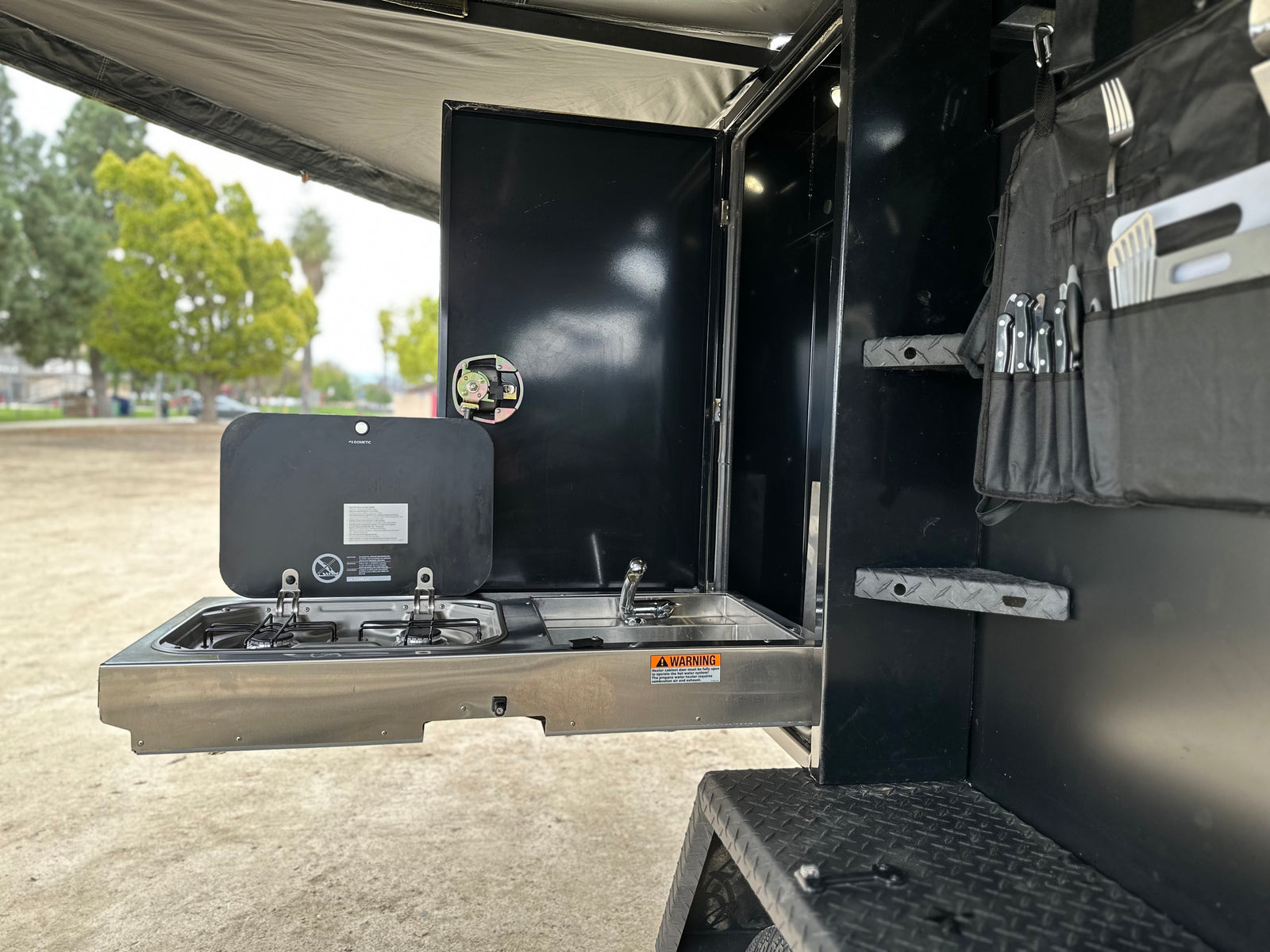 This RV rental features a pull-out Dometic outdoor kitchen with stove, sink, and utensil storage, ideal for camping.