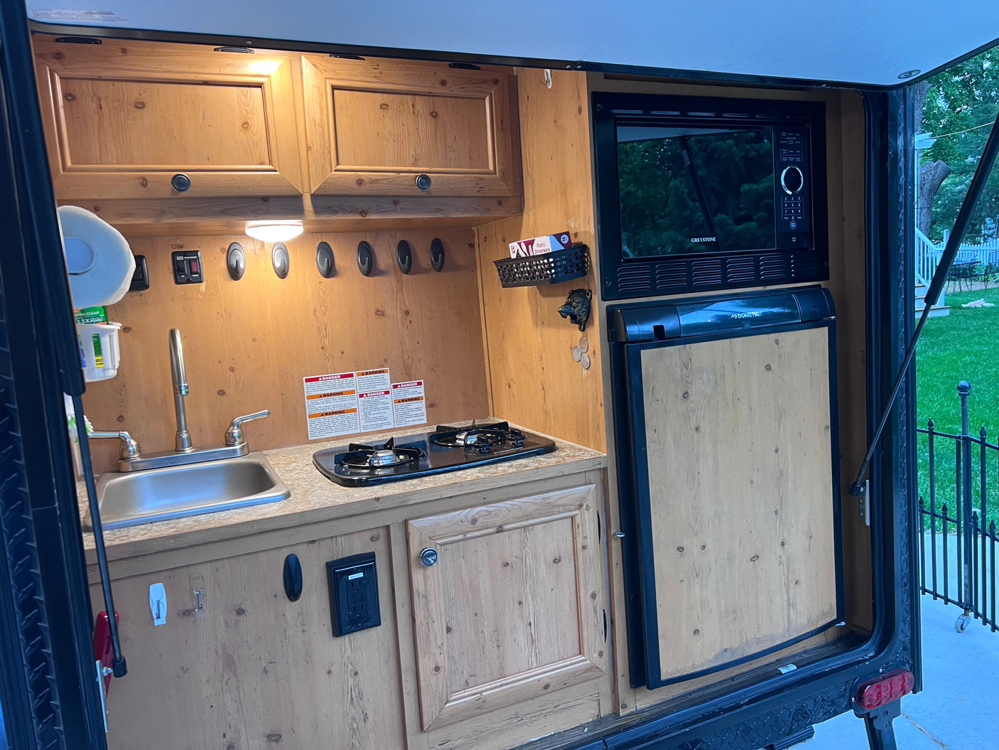 This RV rental features a compact kitchen with a sink, stovetop, microwave, fridge, and wooden cabinets.
