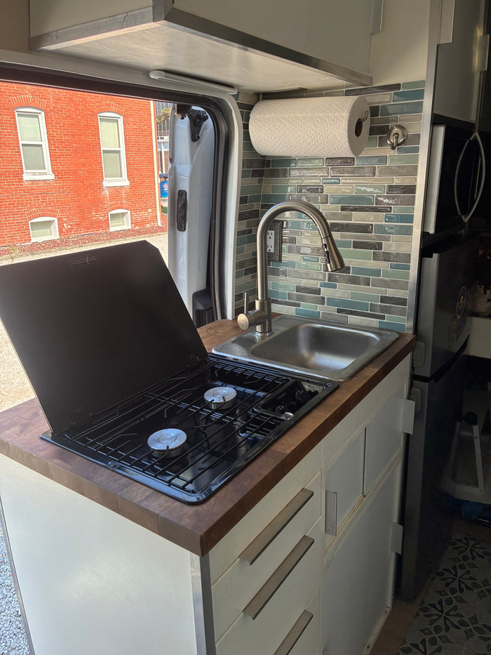Inside an RV rental, a compact kitchen features a two-burner stove, sink, and elegant tile backsplash for cooking on the road.