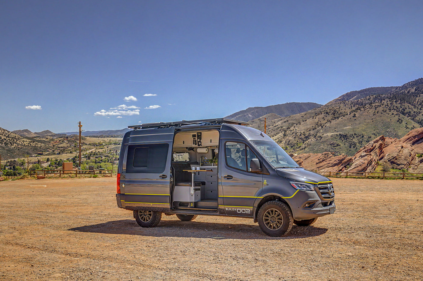 Rugged gray Mercedes Sprinter camper van, an ideal rv rental, with side door open revealing its interior kitchen, set in mountains.