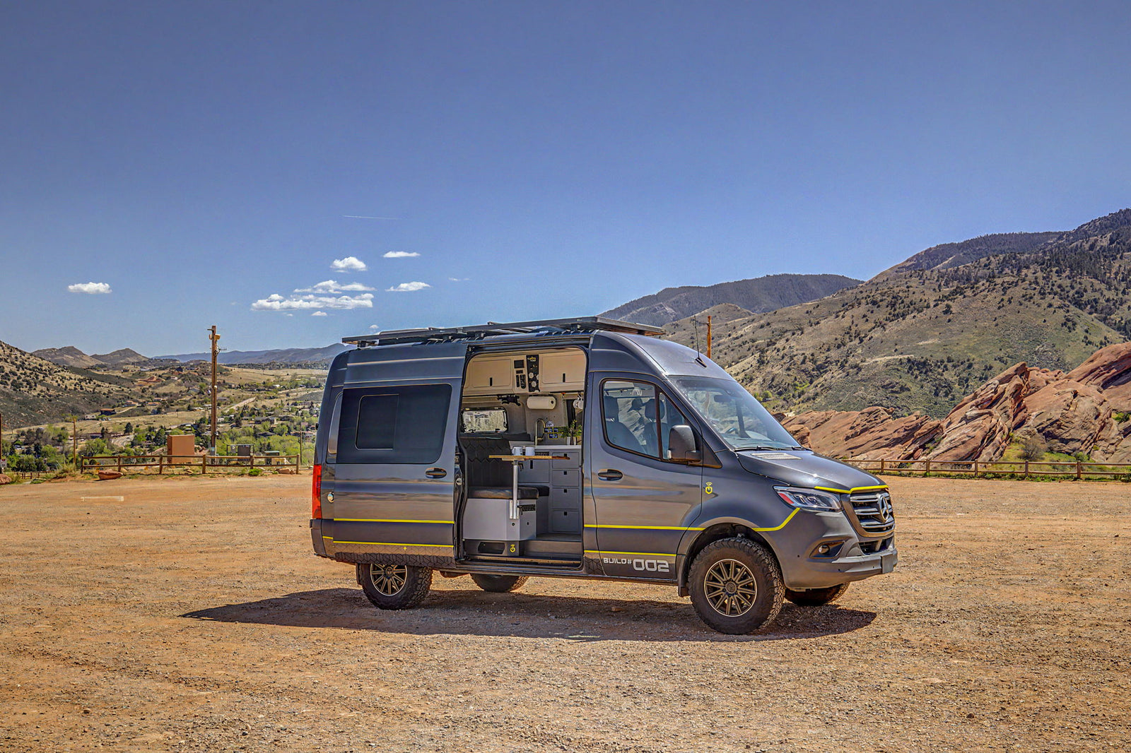 Rugged gray Mercedes Sprinter camper van, an ideal rv rental, with side door open revealing its interior kitchen, set in mountains.