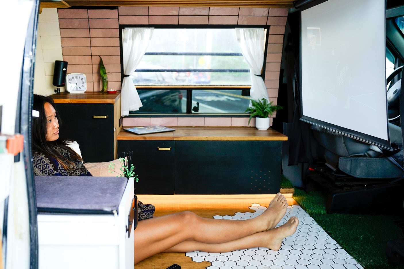A woman relaxes in a comfortable RV rental, enjoying a game projected on a screen in her custom mobile living space.