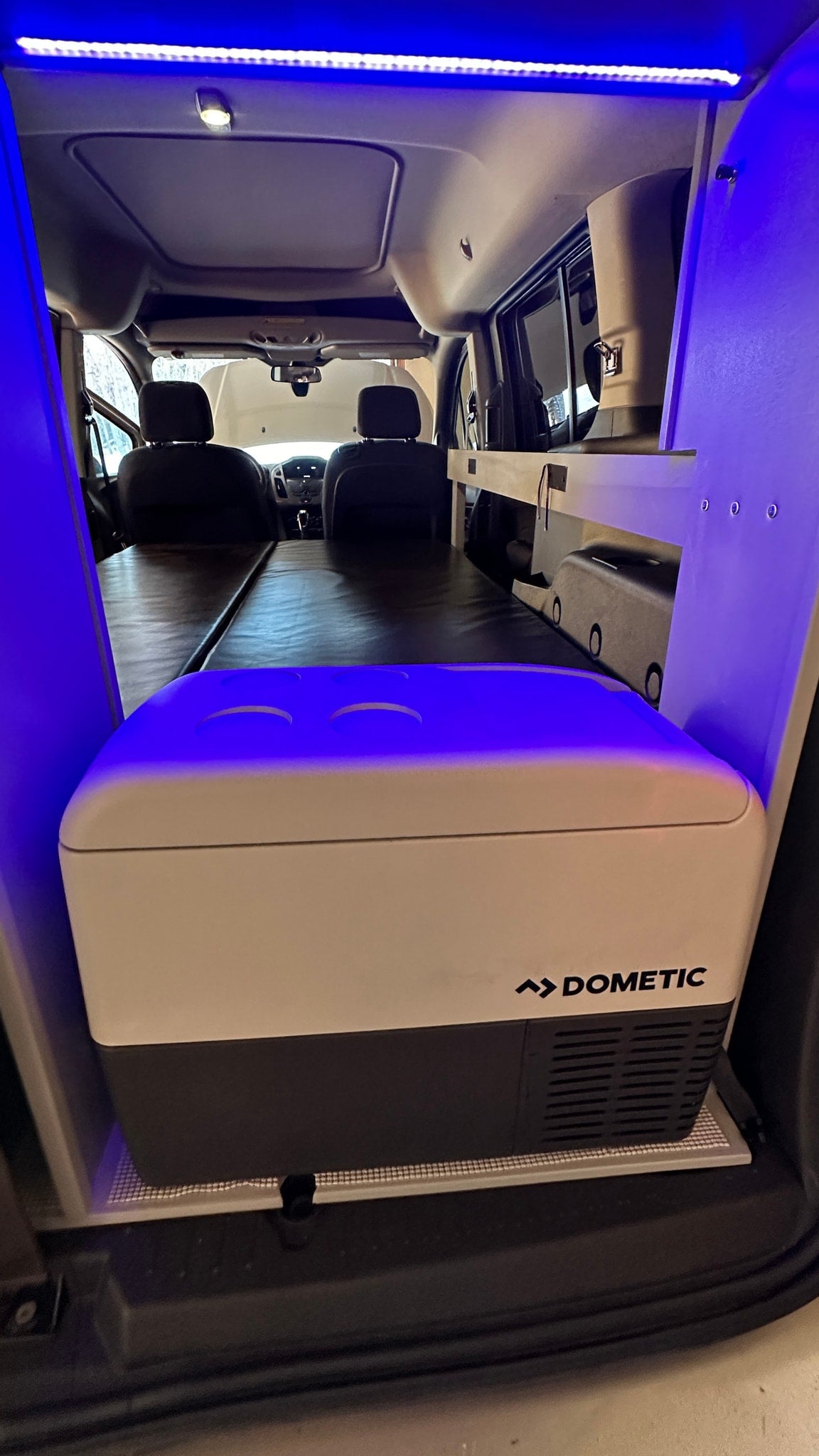 Interior of an rv rental camper van featuring a Dometic fridge, a comfortable sleeping platform, and vibrant blue LED lights. — photo 11