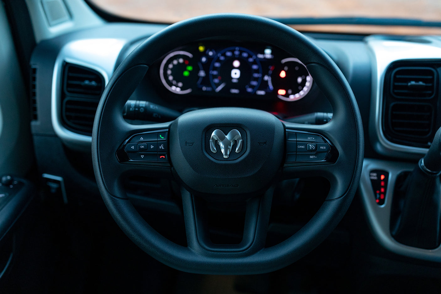 Ram steering wheel and illuminated digital dashboard in an RV rental, showing vehicle controls and gauges.