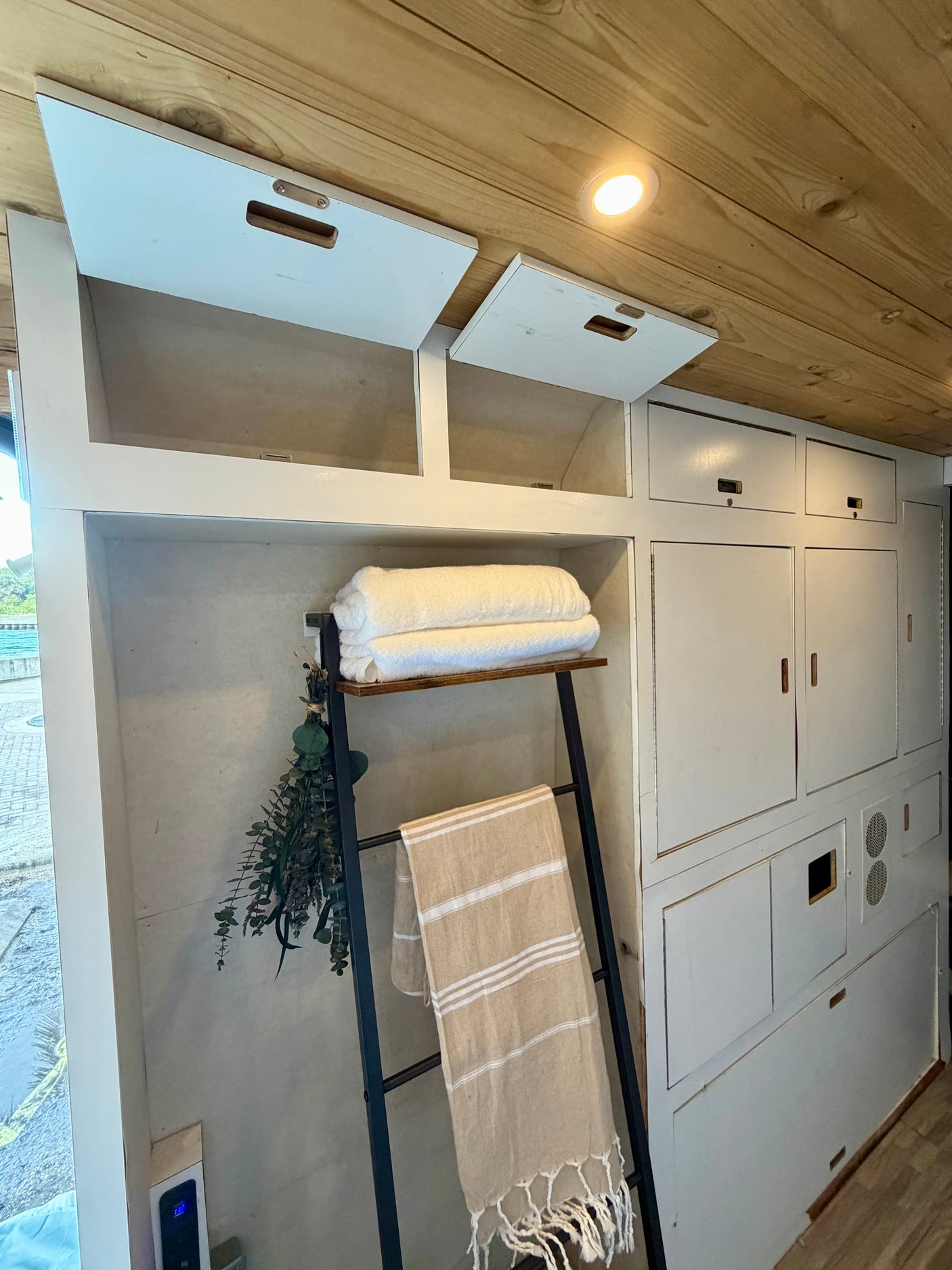 This RV rental interior features minimalist white storage cabinets, warm wooden ceiling, and a practical towel display with fresh linens.