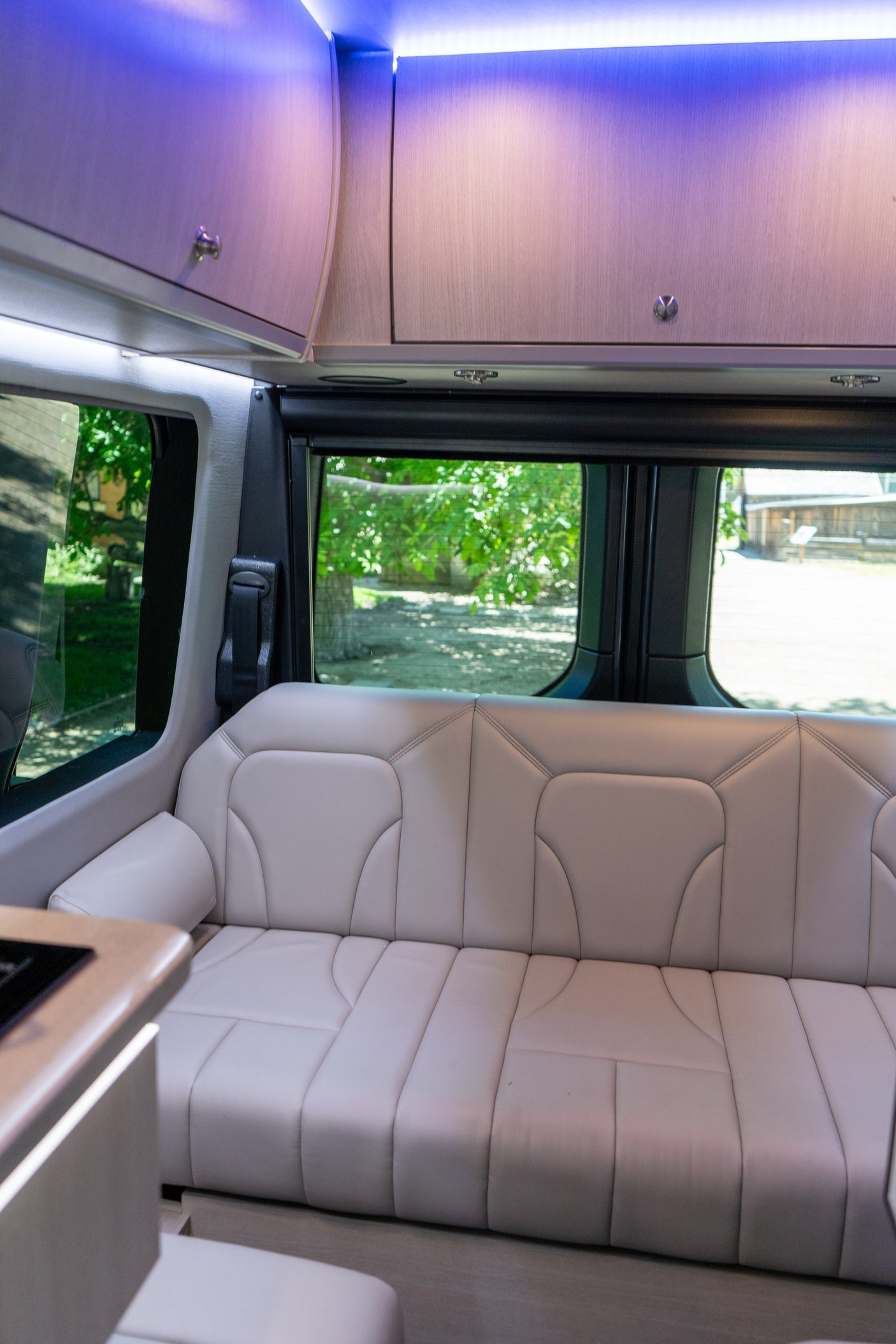 Modern RV rental interior with light-colored bench seating, bright purple overhead lights, and scenic views through the windows.