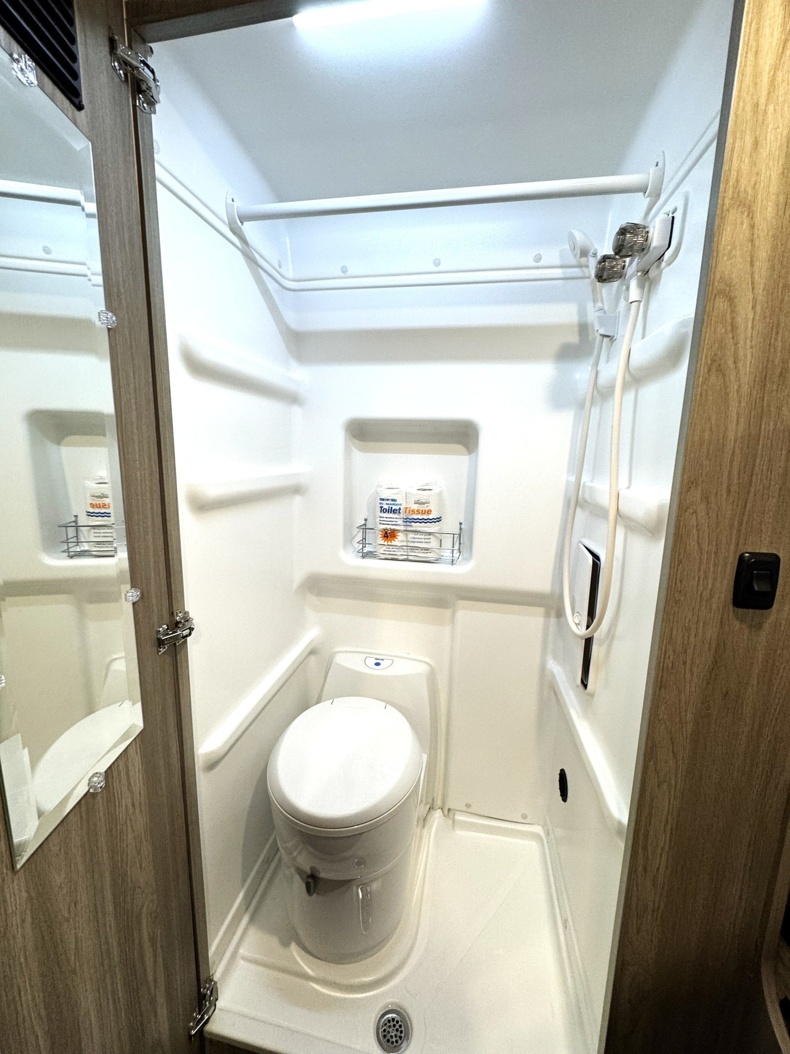 Compact RV rental wet bath featuring a toilet, shower, and storage for toilet paper. Ideal for travel trailer adventures.