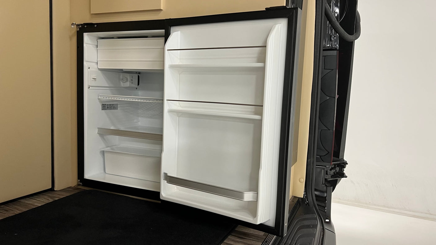 An open, clean, empty refrigerator, likely in an RV rental, showcasing its interior shelves and a small freezer compartment.