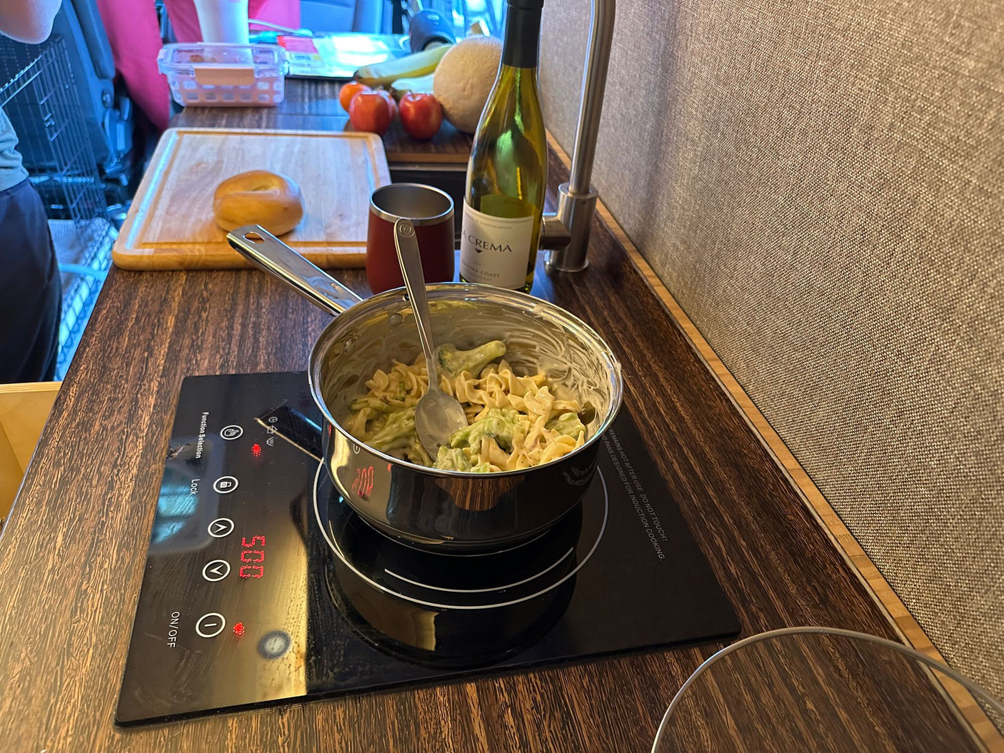 Enjoying a home-cooked meal in an RV rental, with pasta cooking on an induction cooktop, wine, and a bagel.
