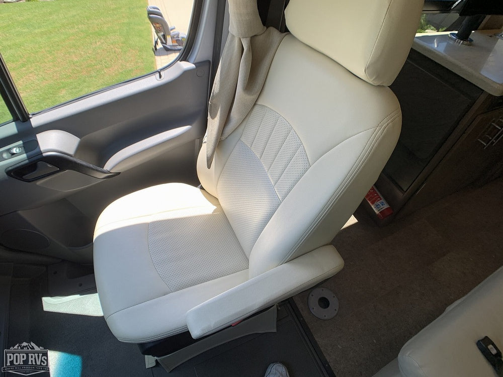 RV rental's white passenger seat with armrests, perforated design, and safety extinguisher. View outside shows green grass.
