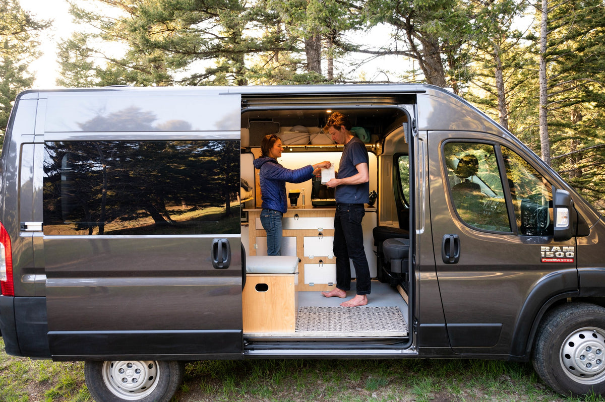 Inside a custom rv rental camper van, a couple stands by the kitchen. Ideal for van life adventures among the trees. — photo 16