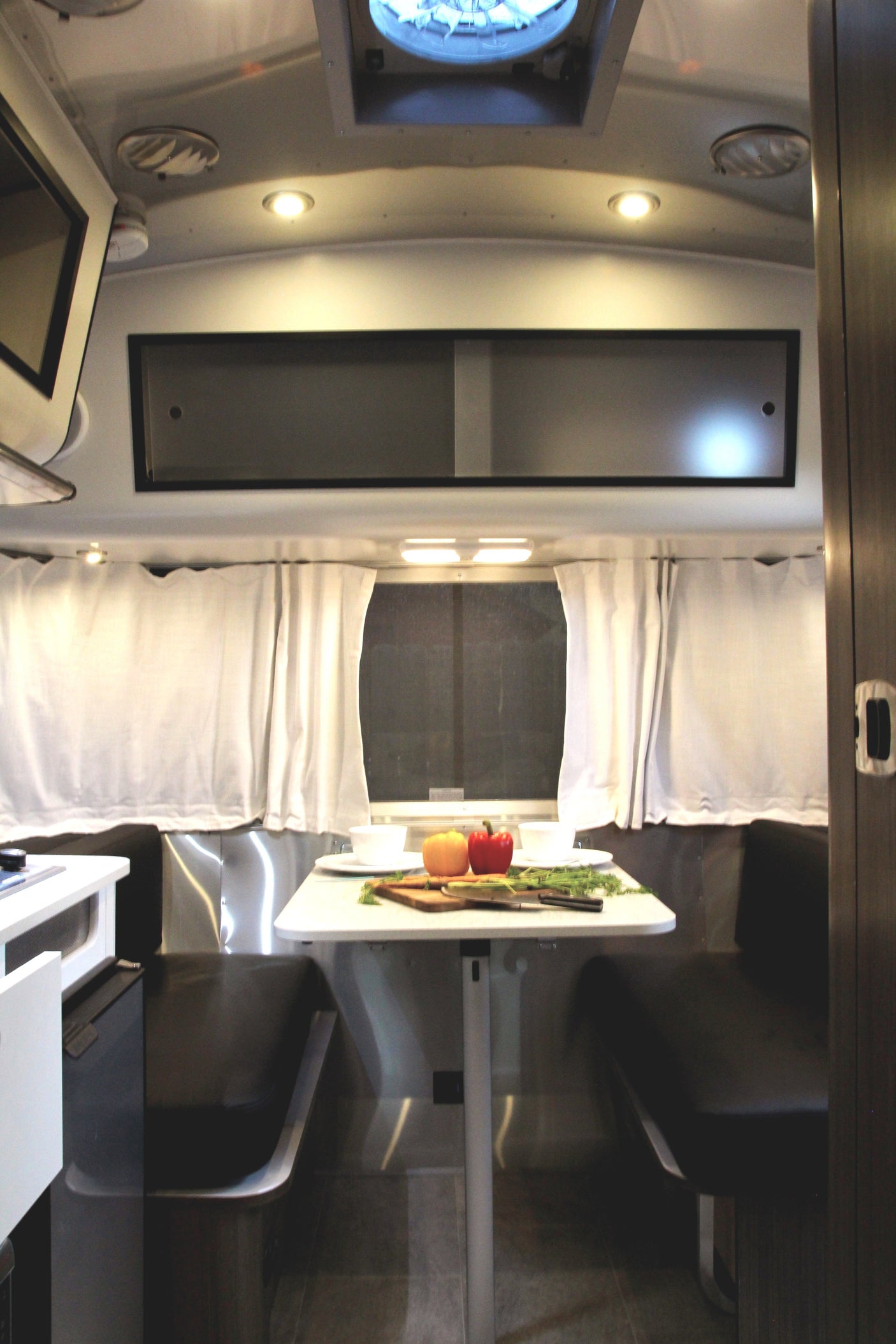 Inside an RV rental: a compact dining nook with a table set for a meal, comfy benches, and sleek overhead storage.