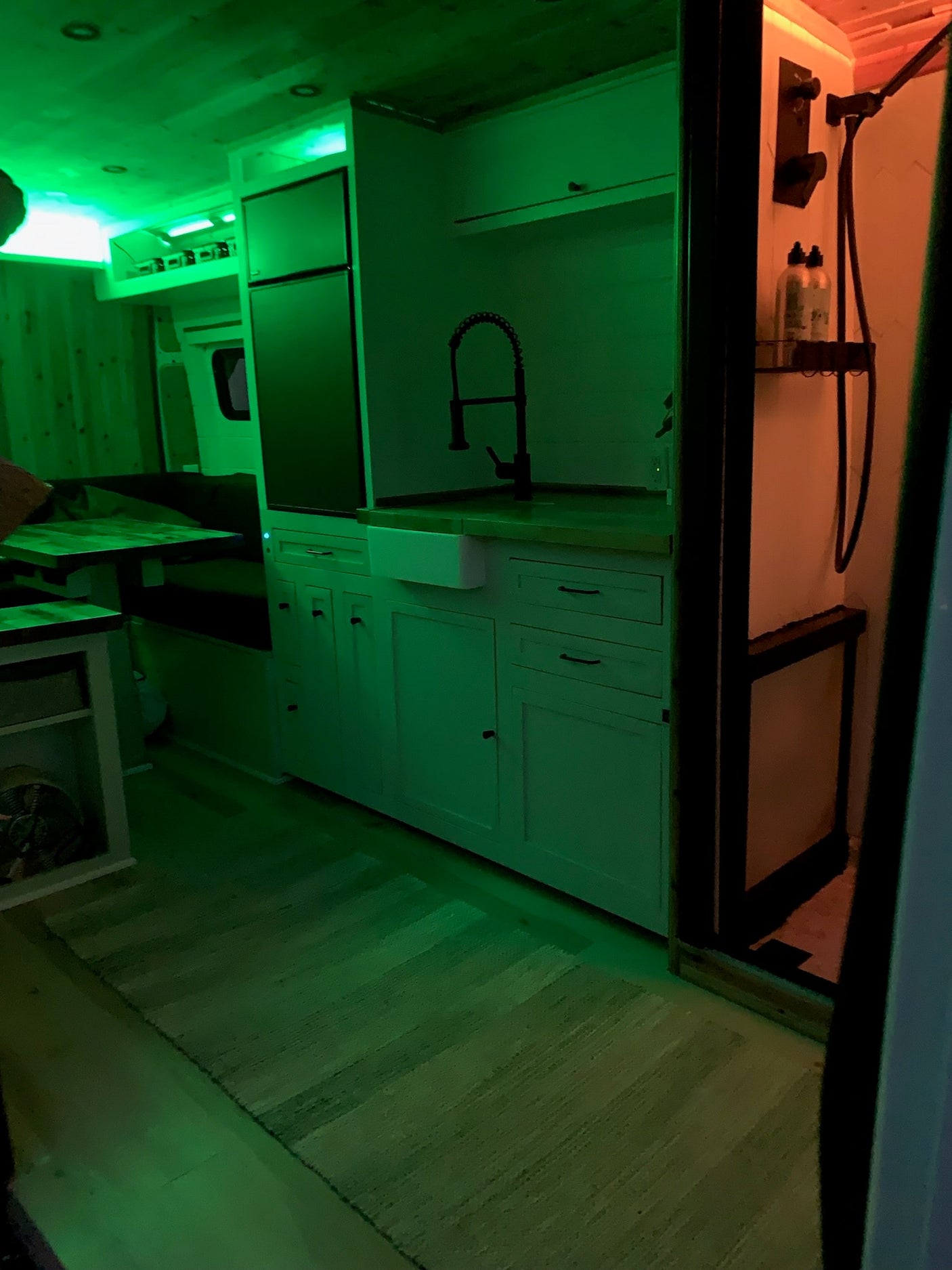Inside this RV rental: a custom kitchen, dining area, and shower, all illuminated by vibrant green and orange lighting.
