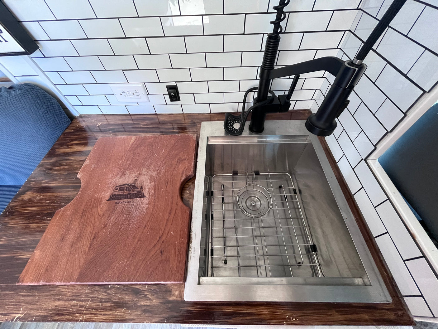 RV rental: Modern kitchen with stainless sink, cutting board, black faucet, and sleek wood counter & subway tile.