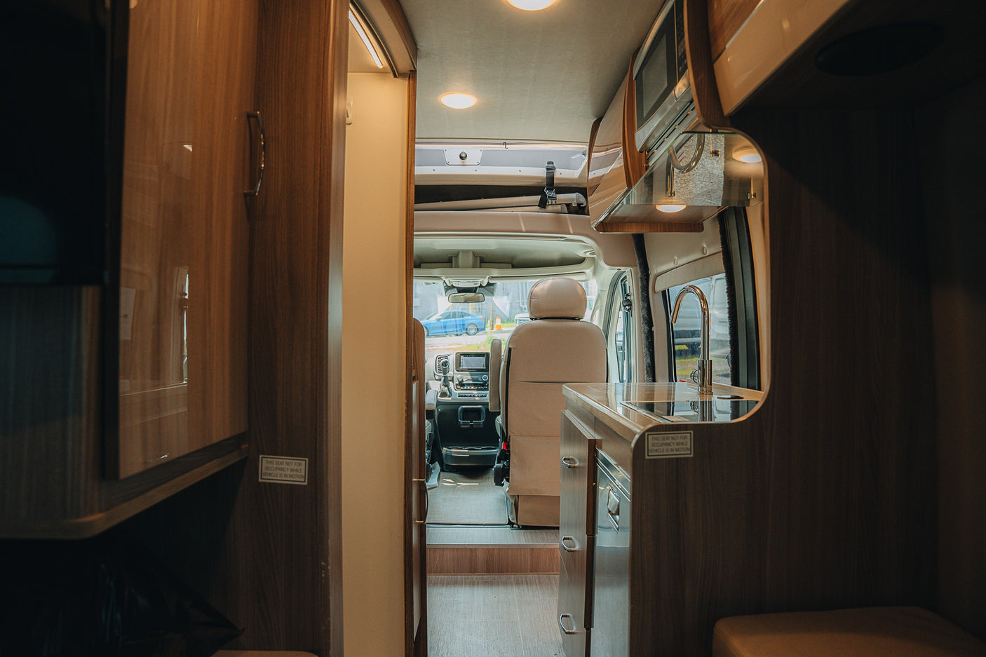Interior of an RV rental: kitchenette with sink, wood cabinets, and clear view to the driver's seat, perfect for road trips.