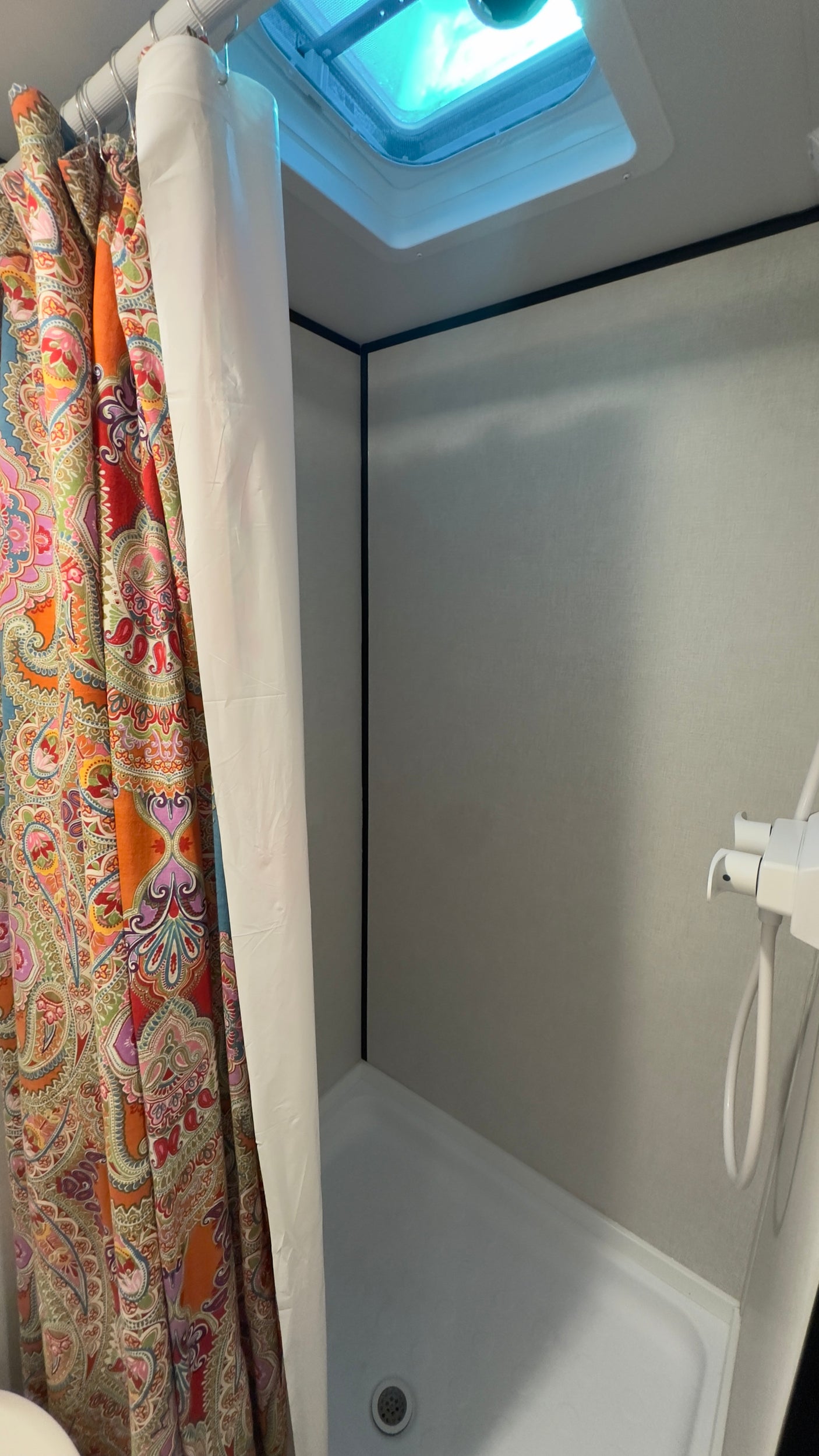 Inside an RV rental: a colorful shower curtain, white liner, shower pan, and overhead skylight.