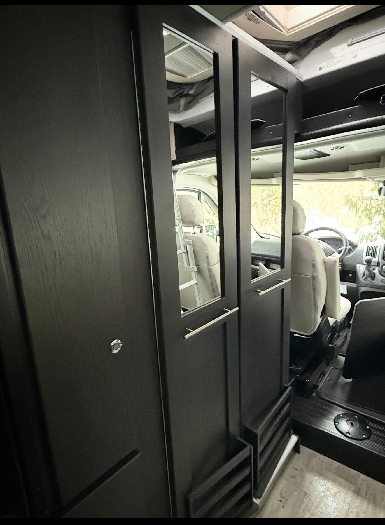 Sleek RV rental interior with dark wood cabinets & mirrored panels, reflecting the front seats of this modern camper van. — photo 8