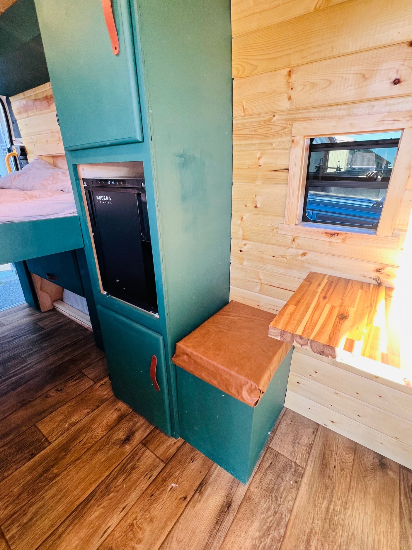 RV rental ready: compact camper van interior with custom green cabinets, BODEGA cooler, bed, and wooden details.
