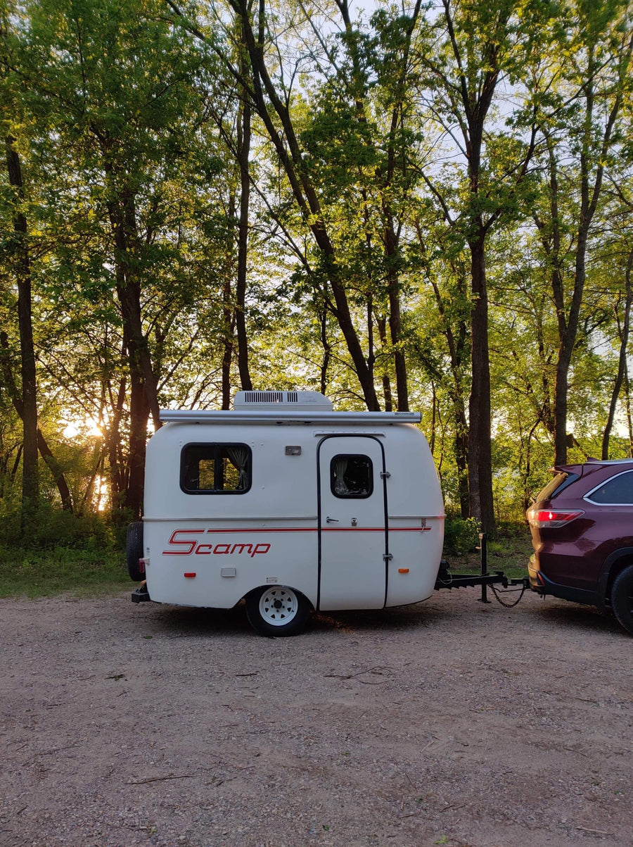 Scamp travel trailer & SUV on gravel. Perfect for an RV rental camping trip in nature at sunset.|Smiling family with baby enjoys an RV rental experience