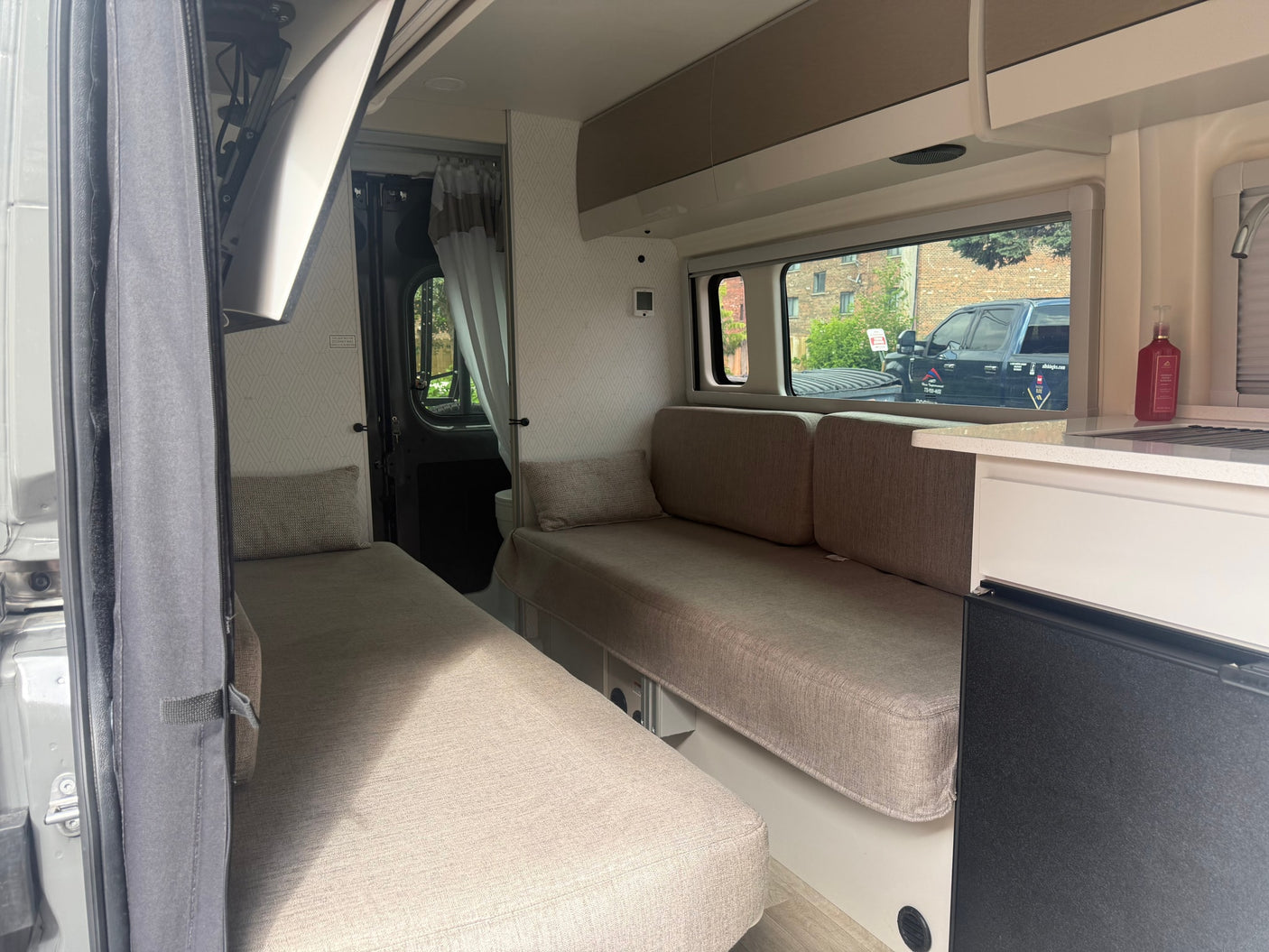 RV rental interior: Bright camper van with two convertible sofa beds, a compact kitchenette, and overhead storage.