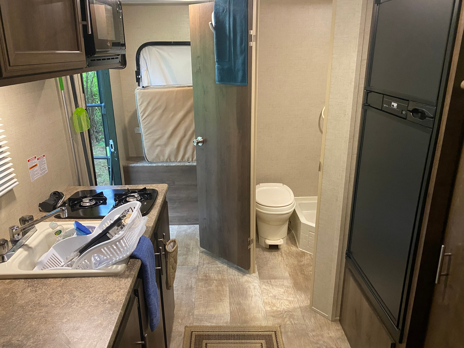 Inside an RV rental, showing the compact kitchen with sink, stove, microwave, a convertible bed, and a small bathroom.