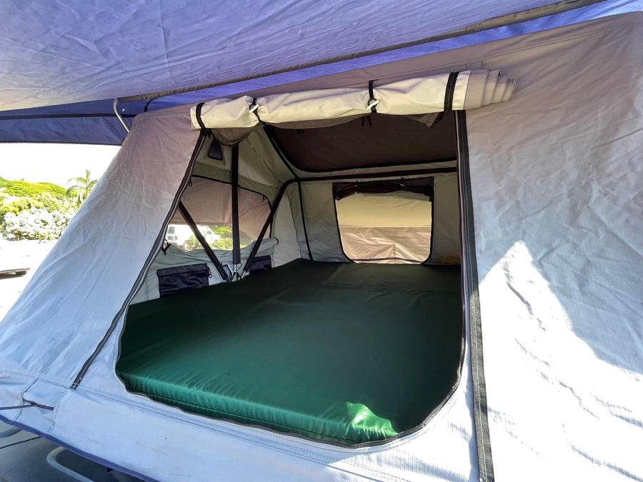 Inside a comfy RV rental rooftop tent, showing the green mattress and spacious sleeping area for adventures.