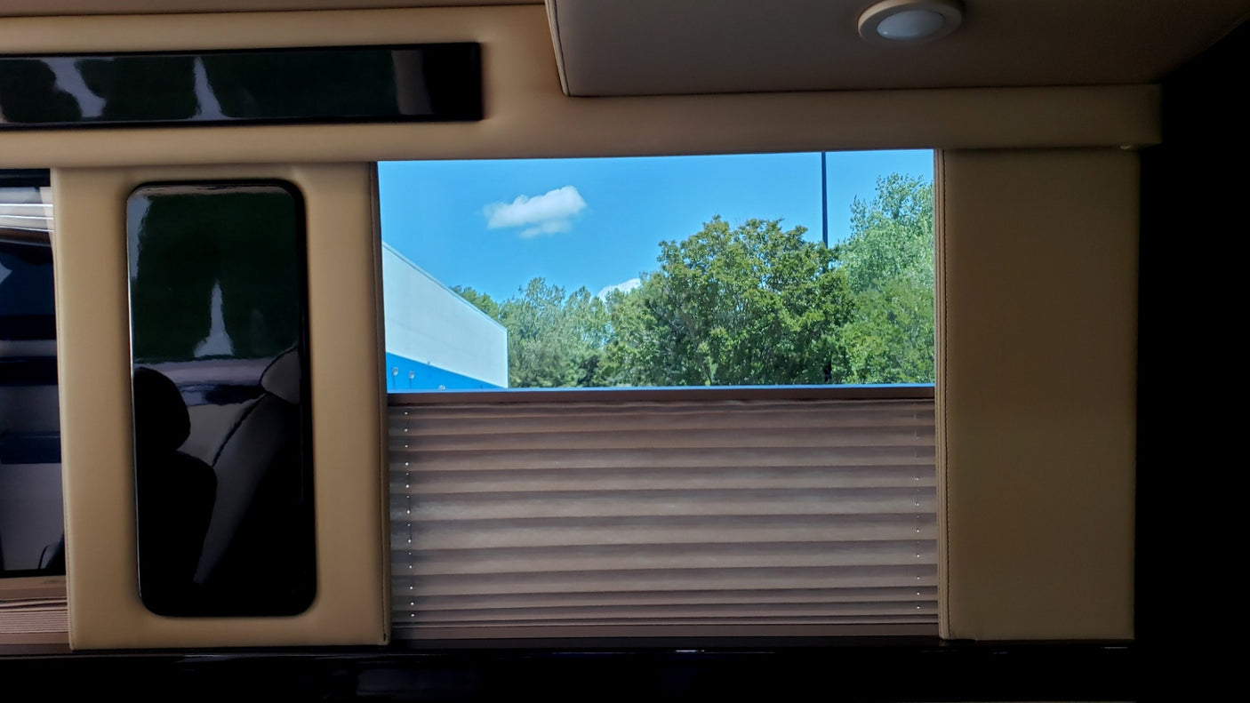 Luxury RV rental interior with a bright window view of sky & trees, a partially drawn blind, and a reflective screen.