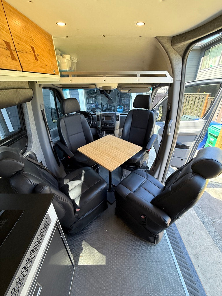 Bright RV rental interior showing versatile seating, a central table, kitchen, and an overhead bed platform.
