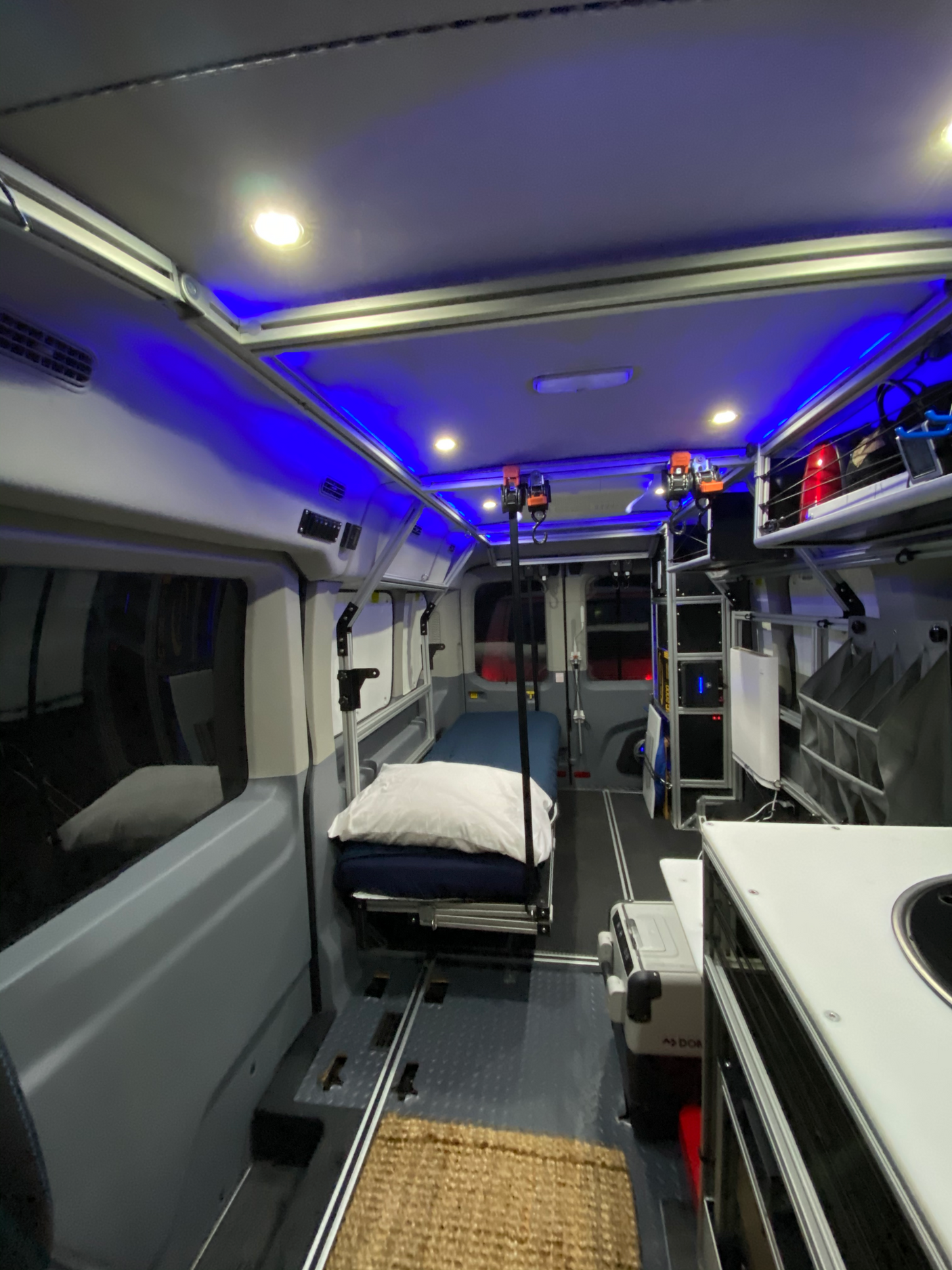 Spacious RV rental interior with a bed, bright and blue ambient lighting, kitchen, and versatile track floor.