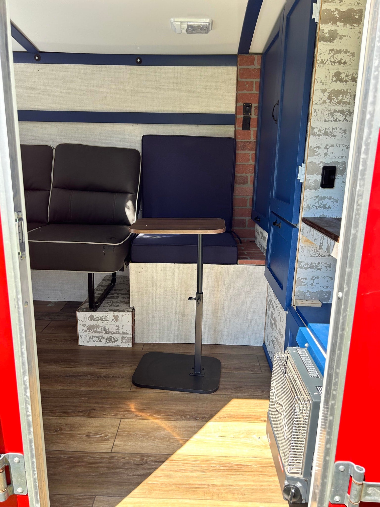 This RV rental's inviting interior features dark seating, blue cushions, an adjustable table, wood-look floor, and brick accents.