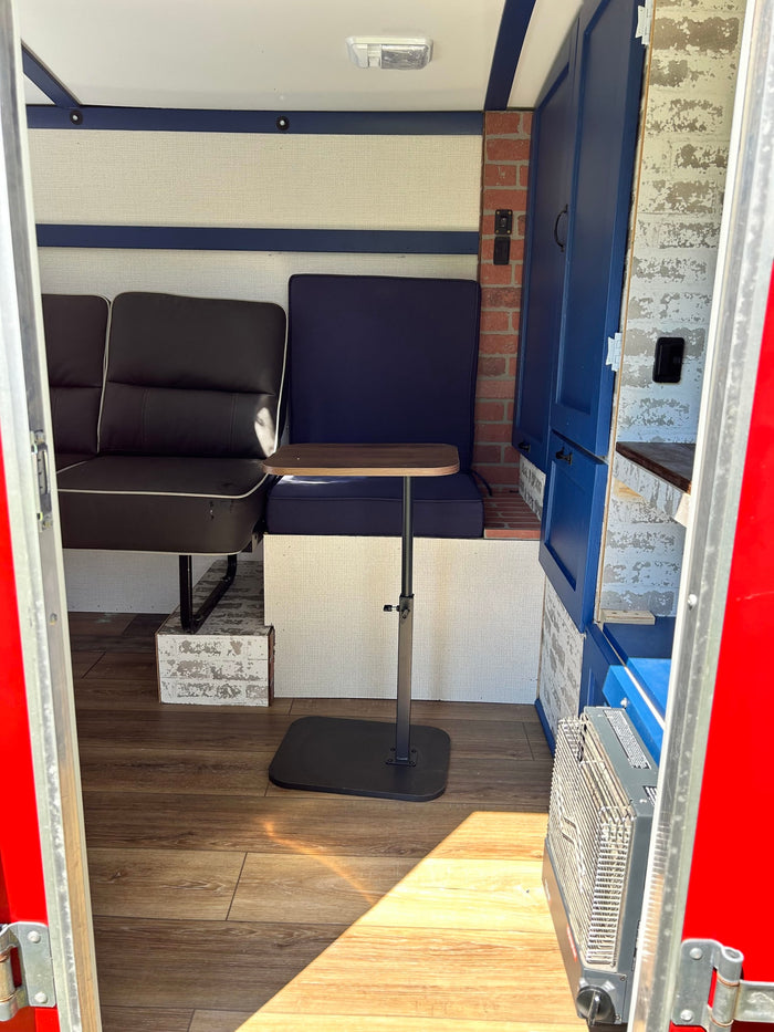 This RV rental's inviting interior features dark seating, blue cushions, an adjustable table, wood-look floor, and brick accents.
