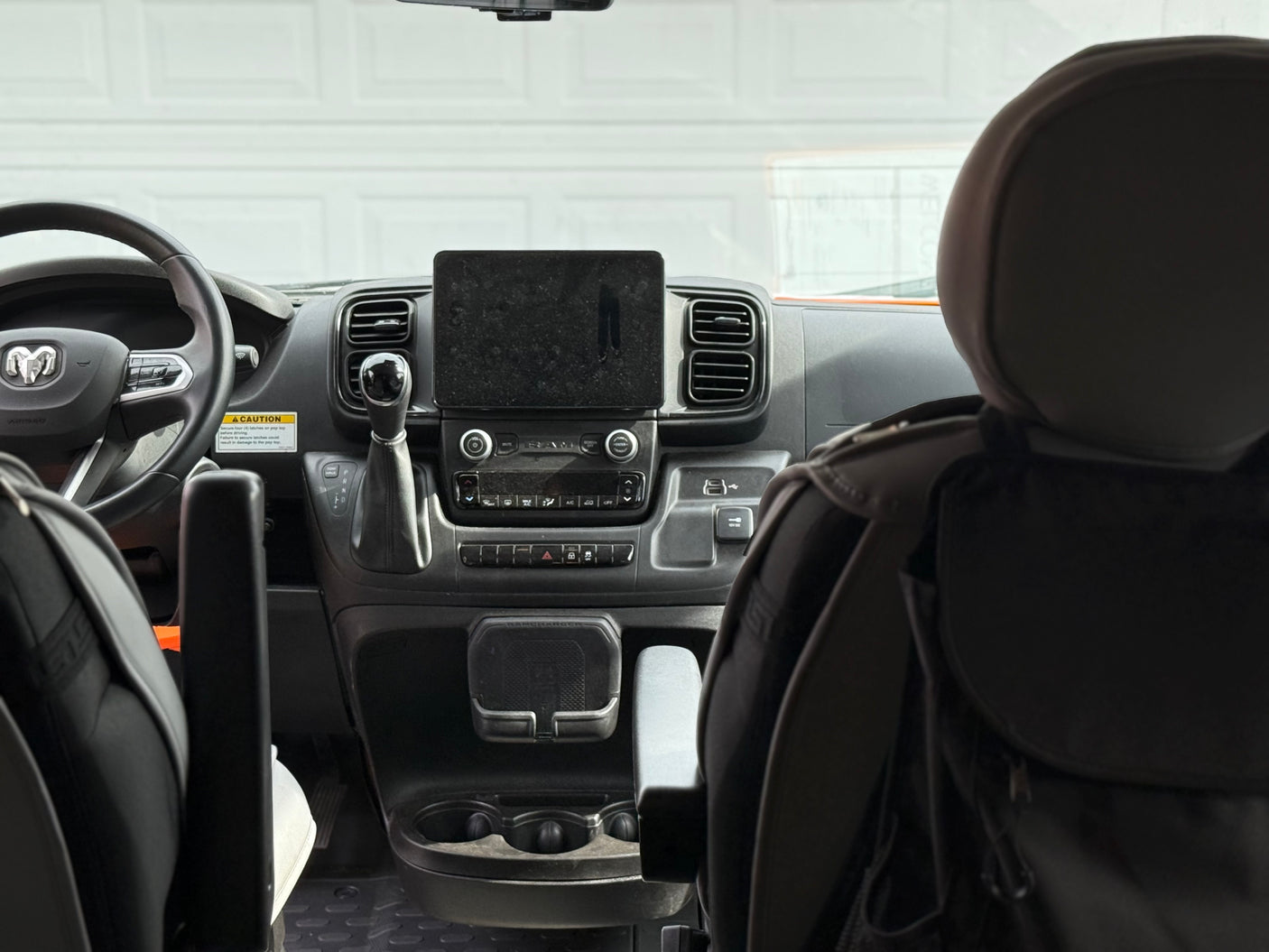 An RV rental van's interior dashboard with steering wheel, gear shift, and tablet mount. Note the pop top caution label.
