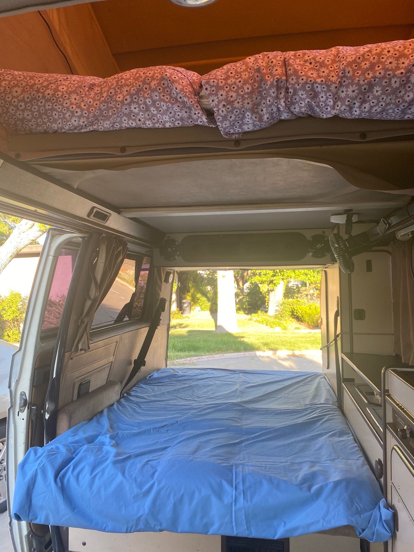and a small fan. A clear view out the windshield.|Experience comfort in an RV rental. This camper van features a green comforter