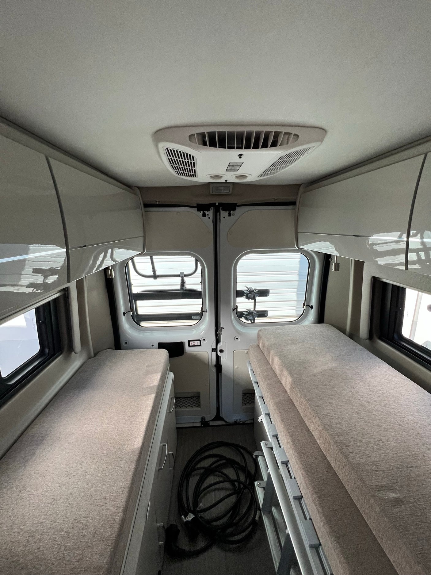Interior view of a modern rv rental, featuring two comfortable beds, overhead storage, and a ceiling AC unit. Ideal for travel.