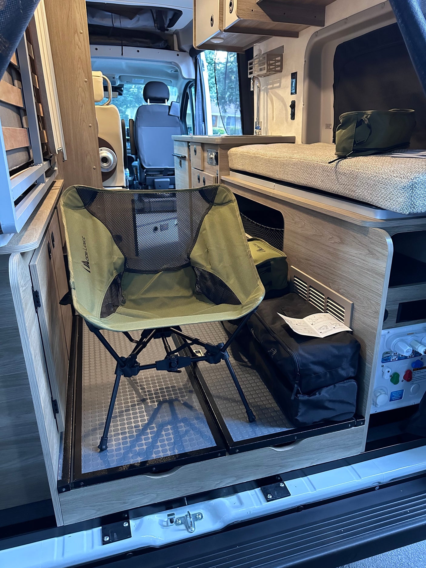 This rv rental interior features a compact, foldable chair on a pull-out tray, next to a bed & kitchenette area.