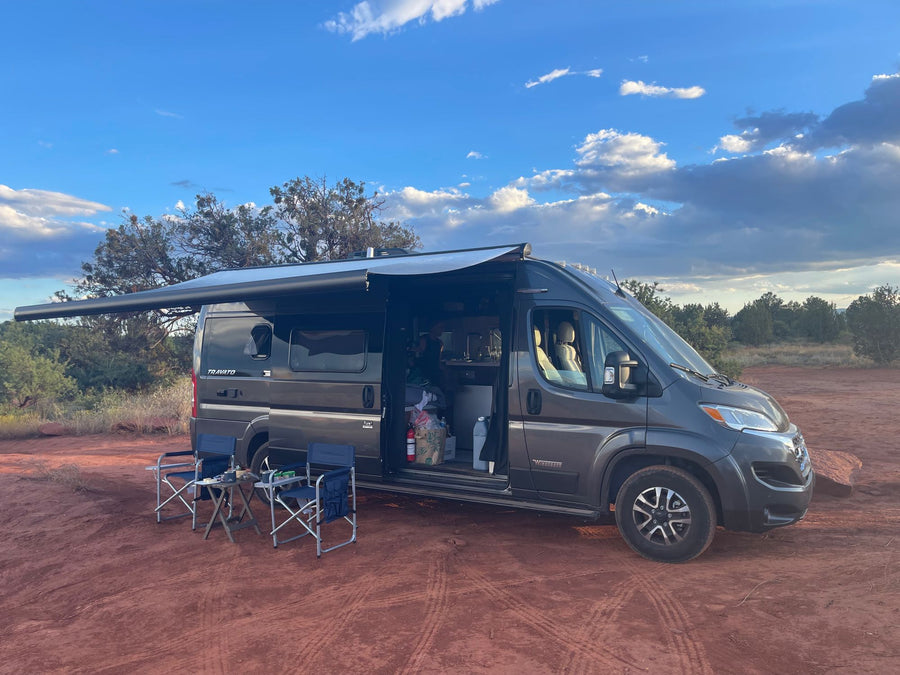 This gray rv rental is perfectly set up for an outdoor adventure. Parked on red earth with awning extended, chairs out, under a blue sky.