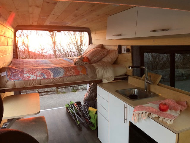 Cozy RV rental interior with a comfy bed, kitchen, and stunning sunset views. Perfect for travel adventures!