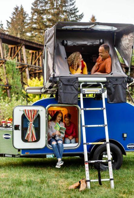 while kids read inside the blue camper.|Family enjoying their RV rental: a blue teardrop trailer with a rooftop tent. Girl is inside the tent