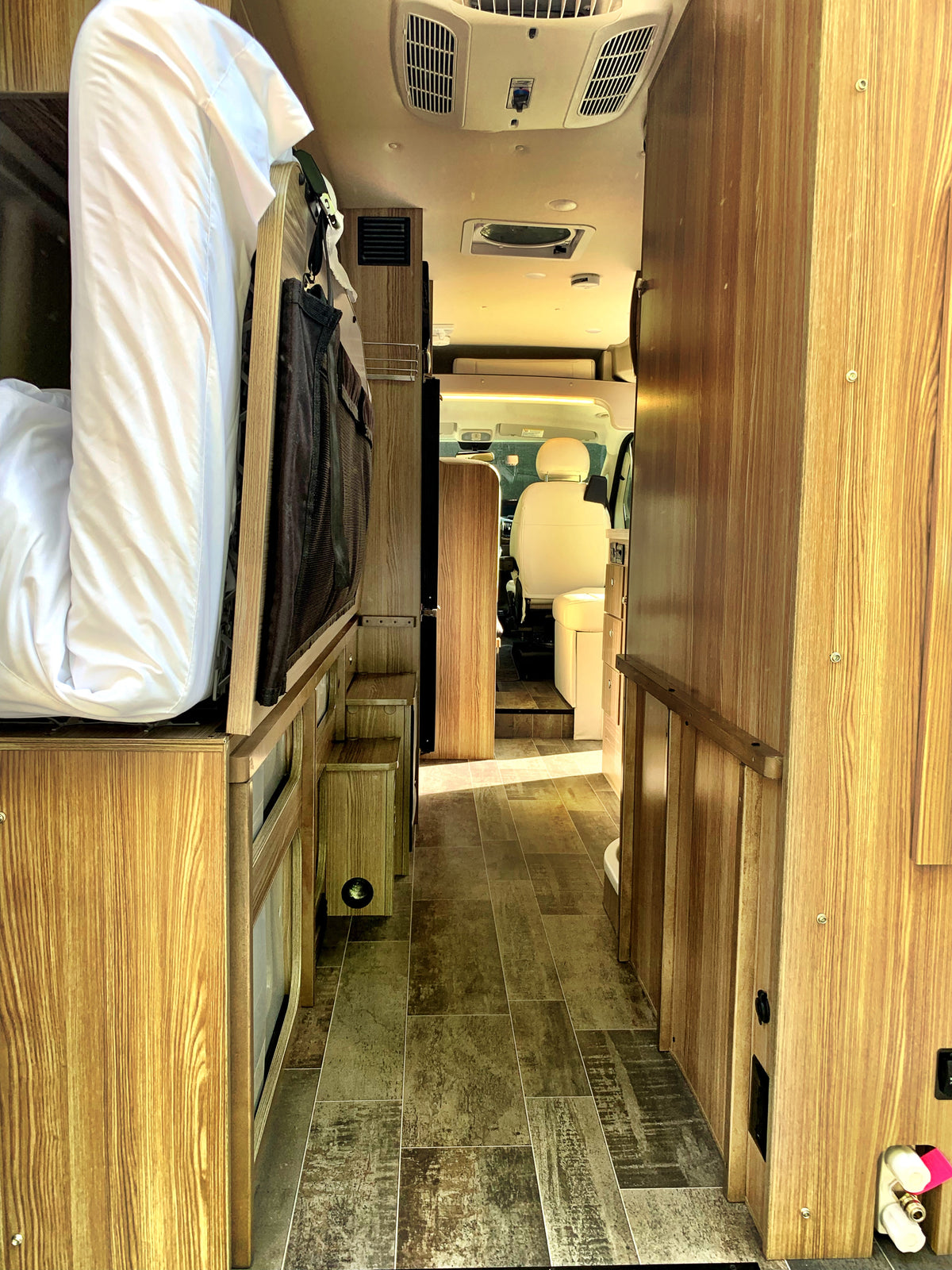 RV rental interior looking forward: bed on left, cabinetry on right, leading to the driver's cabin. — photo 5