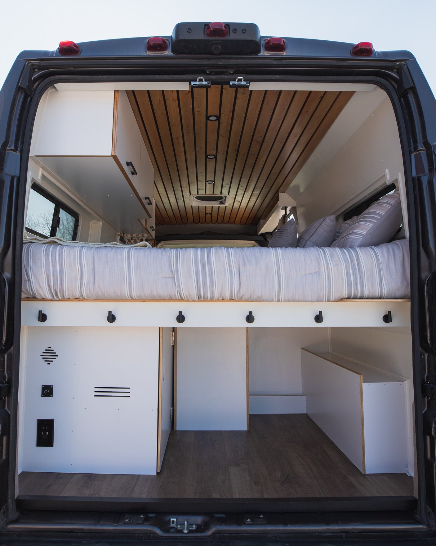 Spacious RV rental interior: cozy bed, smart storage, and wood ceiling details. Perfect van conversion for travel.