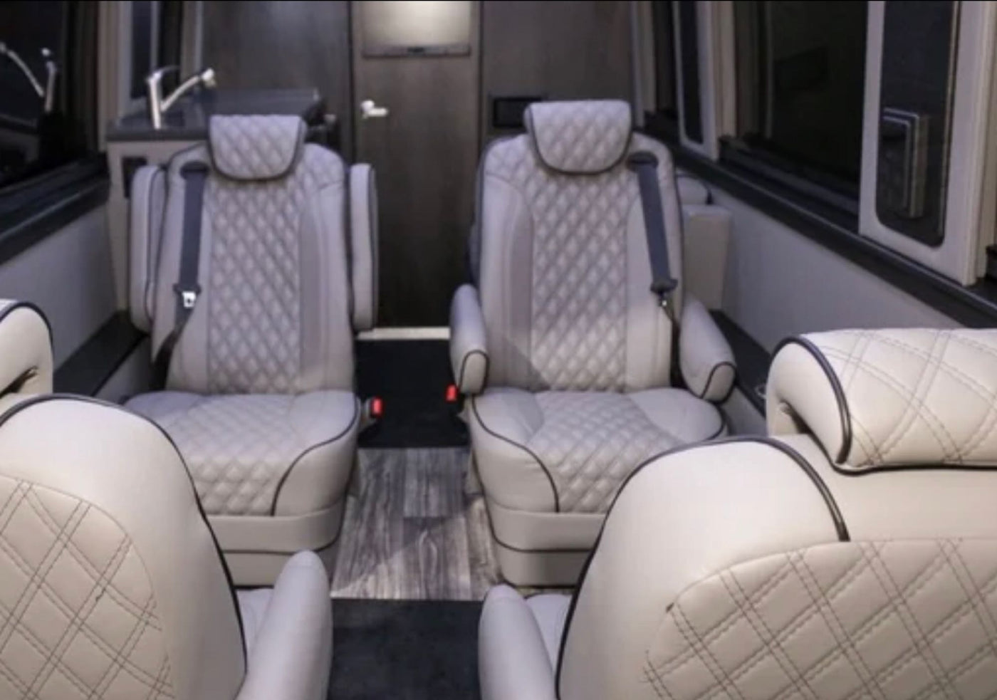 Luxury RV rental interior showcasing light cream quilted seats, modern wood-look flooring, and a compact kitchenette. — photo 7