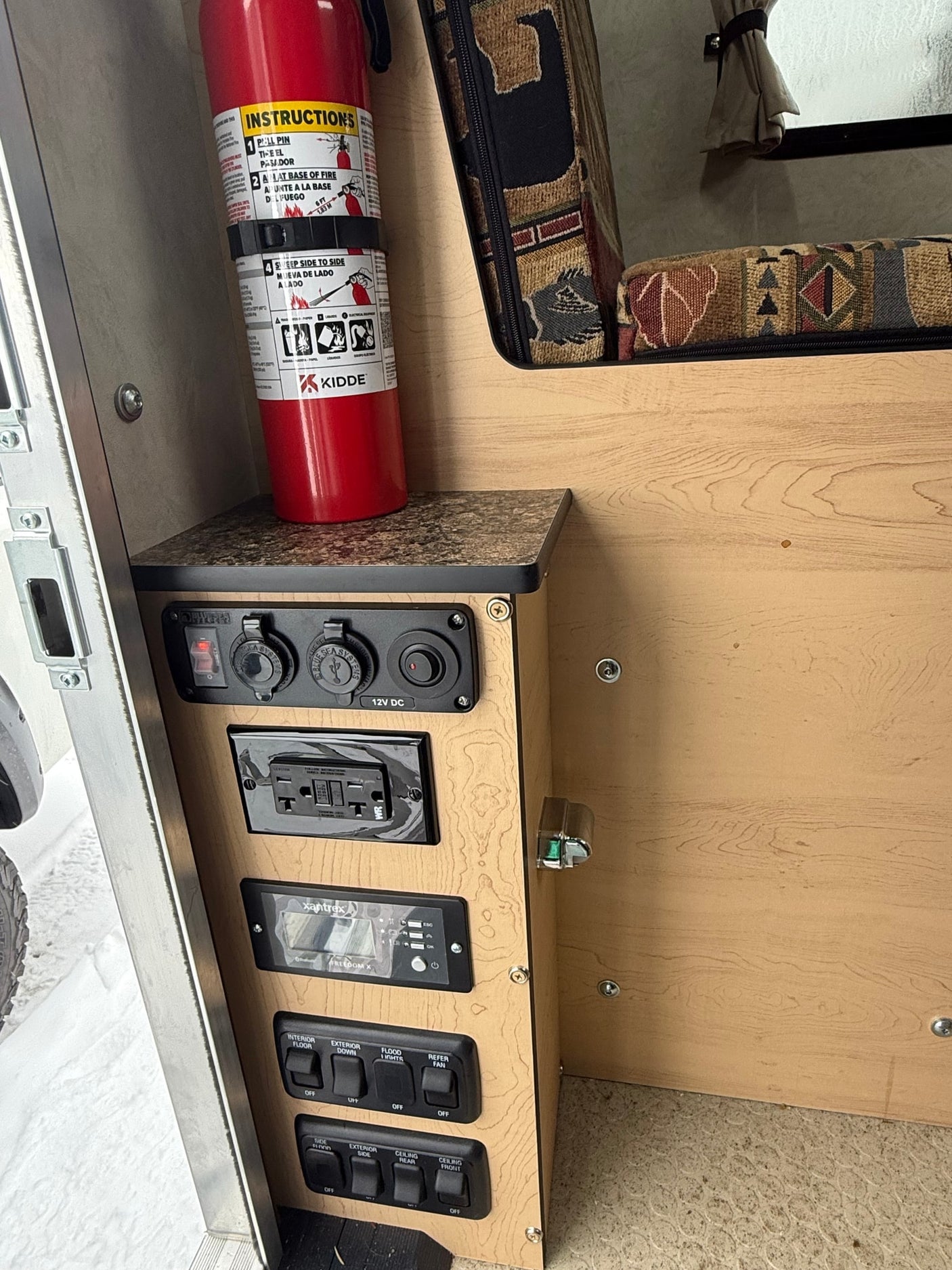 RV rental control panel: electrical outlets, light switches, Xantrex inverter display, and a safety fire extinguisher.